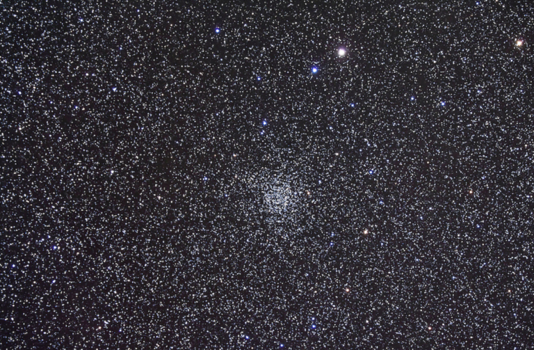 Image of a densely populated star field showing the open star cluster NGC 7789, also known as Caroline’s Rose Cluster, situated in the constellation Cassiopeia. The image is filled with countless small stars, and the central cluster appears as a slightly more concentrated region of stars forming a subtle rose-like pattern. The background is a deep black space with thousands of bright and faint stars of varying colors, including white, blue, and yellow hues.