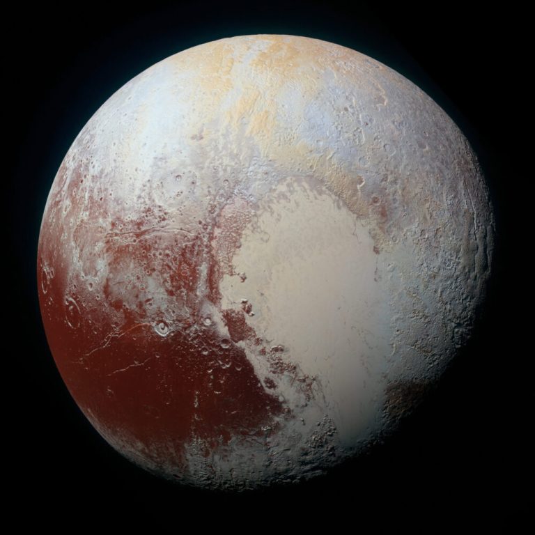 A detailed, full-disk view of a celestial body fills almost the entire frame against a solid black background. The textured surface displays a patchwork of distinct colors, featuring a large, smooth, light cream-colored region in the lower center bordered by heavily cratered, deep rust-red terrain to the left and pale bluish-grey areas near the top and right. Soft lighting across the sphere highlights fine surface crevices and crater rims, creating gentle shadows near the lower-right edge.