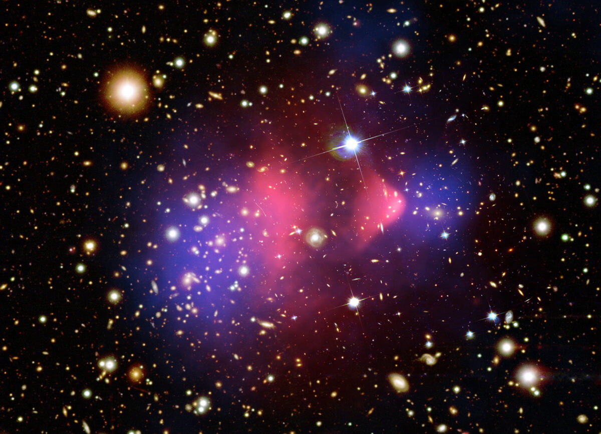 This composite image shows X-rays and visible light from the Bullet Cluster of galaxies, which is made of two separate galaxy clusters colliding. The hot gas associated with the cluster, which comprises most of the normal matter and is visible in X-rays, is colored pink. But the distribution of mass obtained through gravitational lensing is shown in blue — this is the location of the cluster’s dark matter. The disconnect between the two shows that dark matter and normal matter are affected differently by the merger.