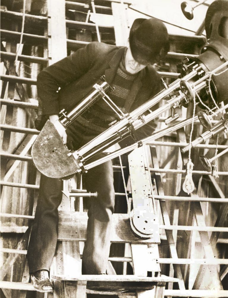Slipher stands with the Brashear spectrograph, mounted on the 24-inch Clark Telescope, with which he made his many spectroscopic discoveries — including his observations of multiple spiral nebulae, most of which were rushing away from Earth at great speed, signaling the expansion of the universe.