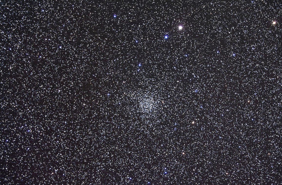 Image of a densely populated star field showing the open star cluster NGC 7789, also known as Caroline’s Rose Cluster, situated in the constellation Cassiopeia. The image is filled with countless small stars, and the central cluster appears as a slightly more concentrated region of stars forming a subtle rose-like pattern. The background is a deep black space with thousands of bright and faint stars of varying colors, including white, blue, and yellow hues.