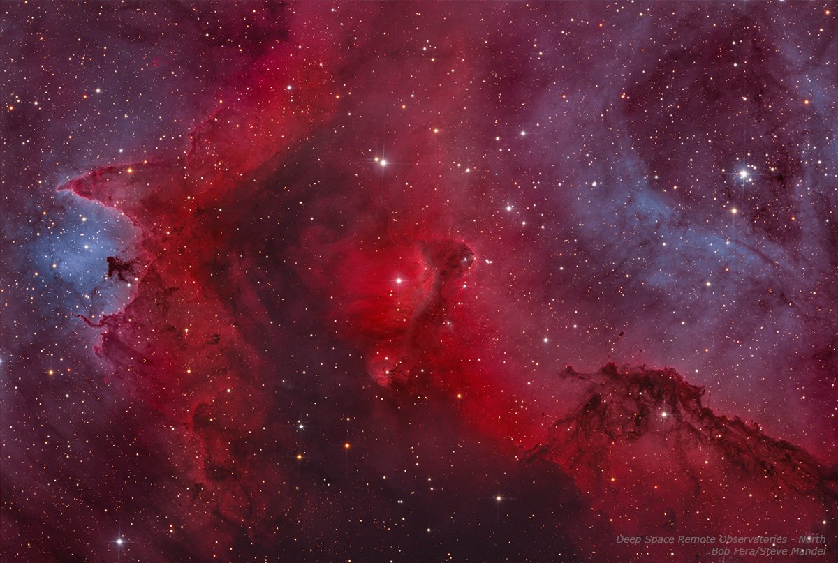 Image of the Soul Nebula, a vast red emission nebula in the constellation Cassiopeia. Bright tendrils of glowing hydrogen gas weave around dark dust lanes, with embedded star clusters illuminating the cloud from within.