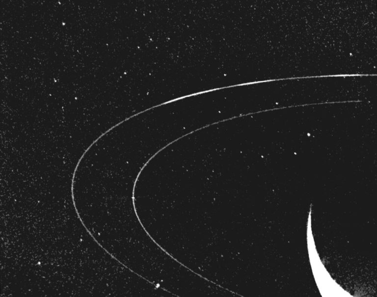 A monochrome, high-contrast image shows two thin, glowing white concentric rings arching across a black, star-speckled background. In the lower-right corner, a bright, solid white crescent curves upward toward the inner ring. Tiny, distant points of white light dot the dark space inside and around the rings, giving the scene high visual contrast.
