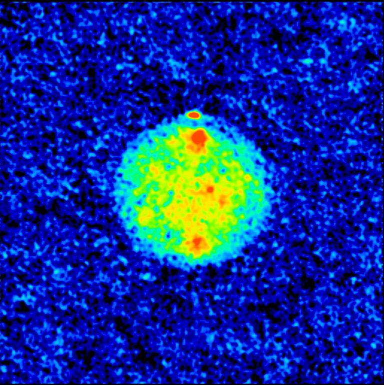 A bright, pixelated circle of mottled yellow and green glowing hues sits centered against a dark, speckled blue-and-black background. Small red-orange spots mark the top, bottom, and center of the bright sphere, with a tiny, isolated red dot floating just off its top edge. High contrast separates the vibrant yellow-green disc from the surrounding cool-toned background.