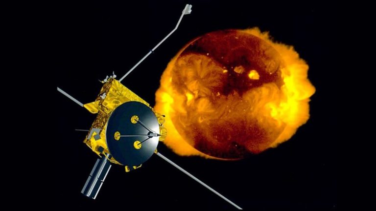 An illustration shows a boxy, gold-foil-wrapped spacecraft with a large black dish antenna on the left, positioned in front of a glowing, fiery sphere on the right against a solid black space background. The central sun-like orb ranges in color from dark, swirling reddish-browns to intense, bright yellow flare-like bursts around its edges. Several thin, metallic booms and antenna rods extend outward diagonally from the main body of the satellite, creating strong geometric contrast with the soft, fiery texture behind it.