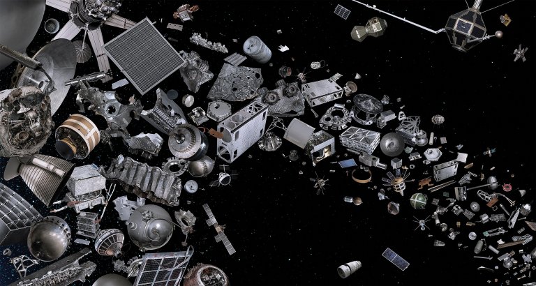 A dense cluster of silver and gray spacecraft components, rocket parts, and satellite fragments floats against a black starfield, packed tightly on the left side of the frame and thinning into scattered individual pieces toward the right. The objects range from large cylindrical rocket stages and solar panel arrays to small bolts and twisted metal fragments.