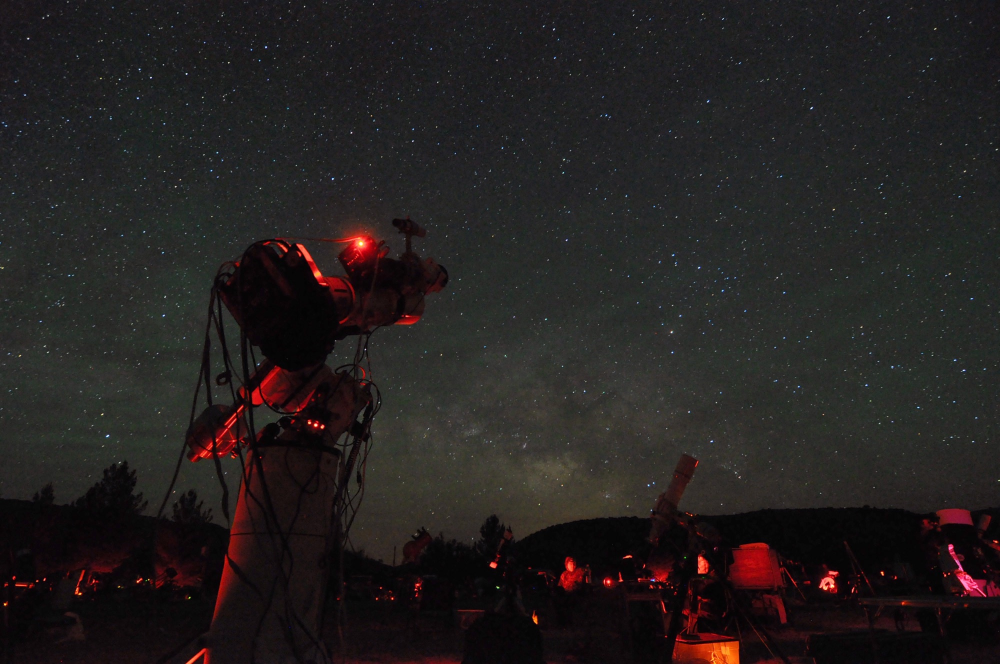 Amateur astronomers gathered at a star party under the Milky Way, observing with red lights