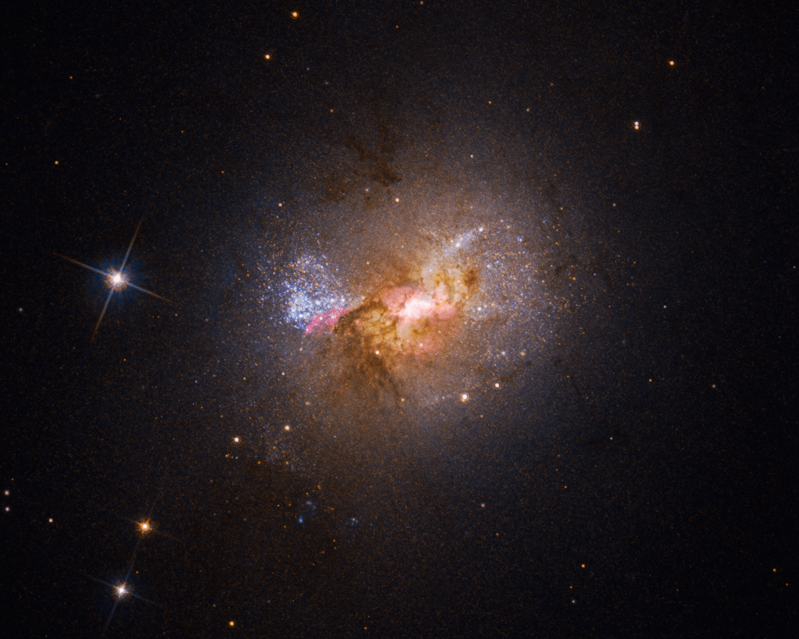 Hubble Space Telescope image of an irregular dwarf galaxy showing bright blue star clusters, pink star-forming regions, and a dusty golden core against a black starfield.