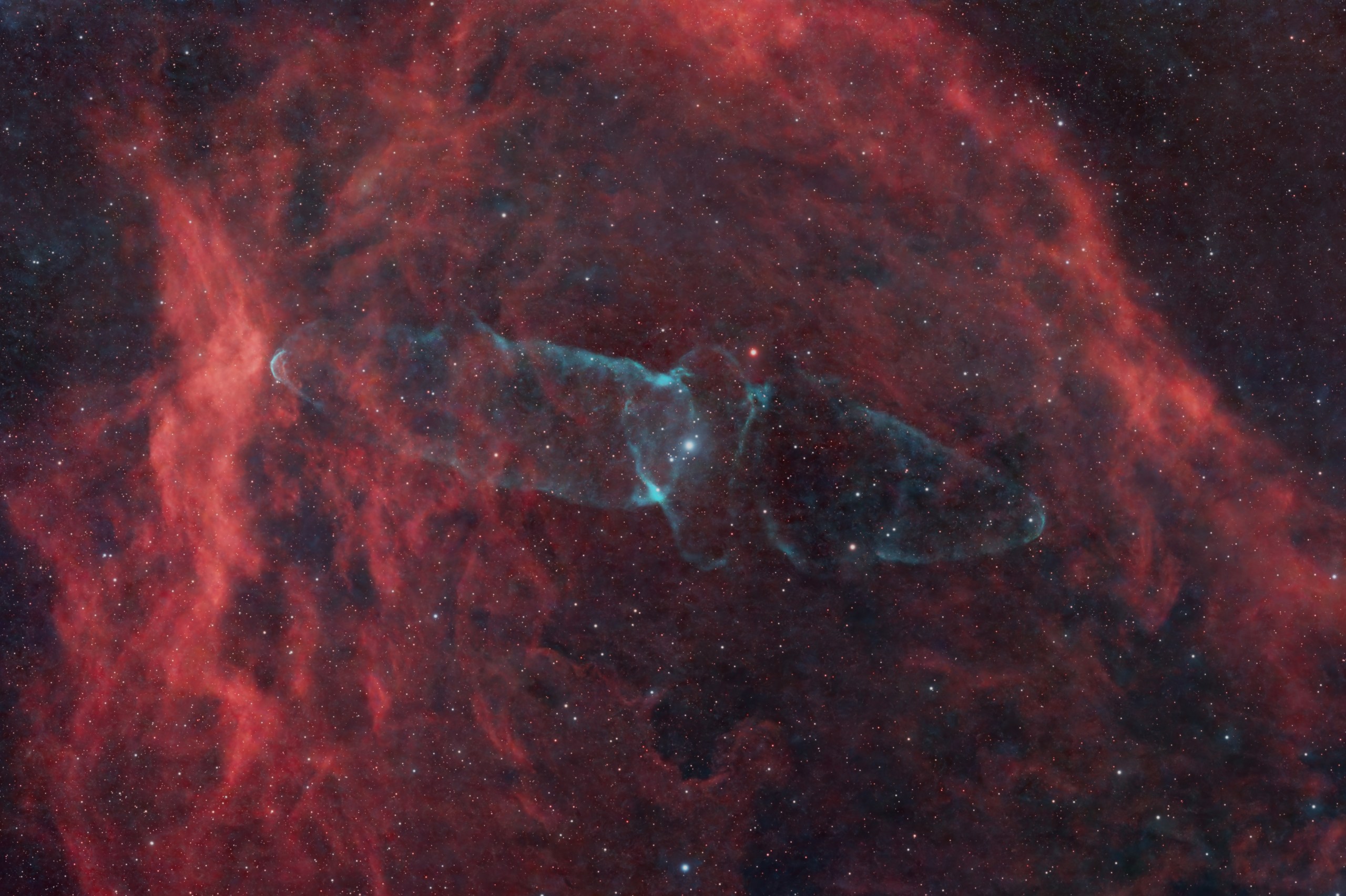 A faint blue-green cloud shaped like a squid stretches across the center of the frame, with two tapering lobes reaching left and right from a brighter, knotted middle. It floats against a much larger backdrop of deep red gas that fills the image in wispy, billowing curtains. Scattered white and pale-blue stars dot the scene.