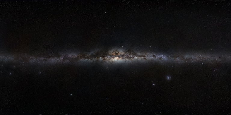 A 360-degree panoramic view of the Milky Way galaxy stretching horizontally across the frame as a bright, glowing band of stars and dust. The galactic center is visible near the middle, dense with warm orange and brown dust lanes and bright star clusters. The surrounding sky is deep black, dotted with individual stars and a few faint nebulae and satellite galaxies visible in the lower portion of the image.