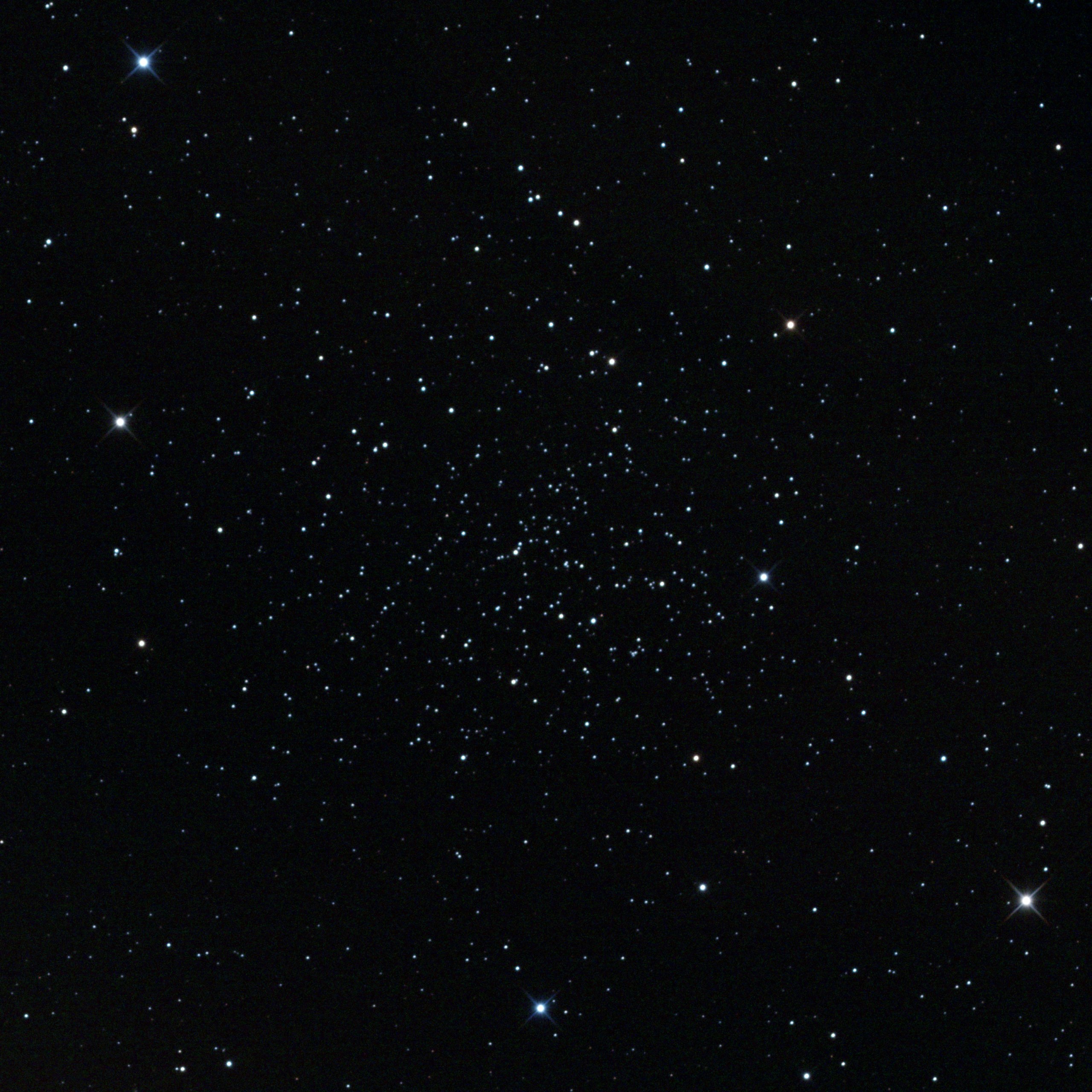 A telescope image of NGC 188, an ancient open star cluster in the constellation Cepheus. Hundreds of faint white and blue-white stars are loosely scattered against a black background, with a few brighter foreground stars visible around the edges.