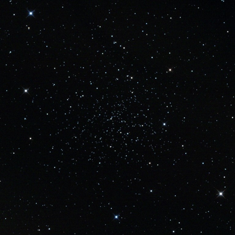 A telescope image of NGC 188, an ancient open star cluster in the constellation Cepheus. Hundreds of faint white and blue-white stars are loosely scattered against a black background, with a few brighter foreground stars visible around the edges.