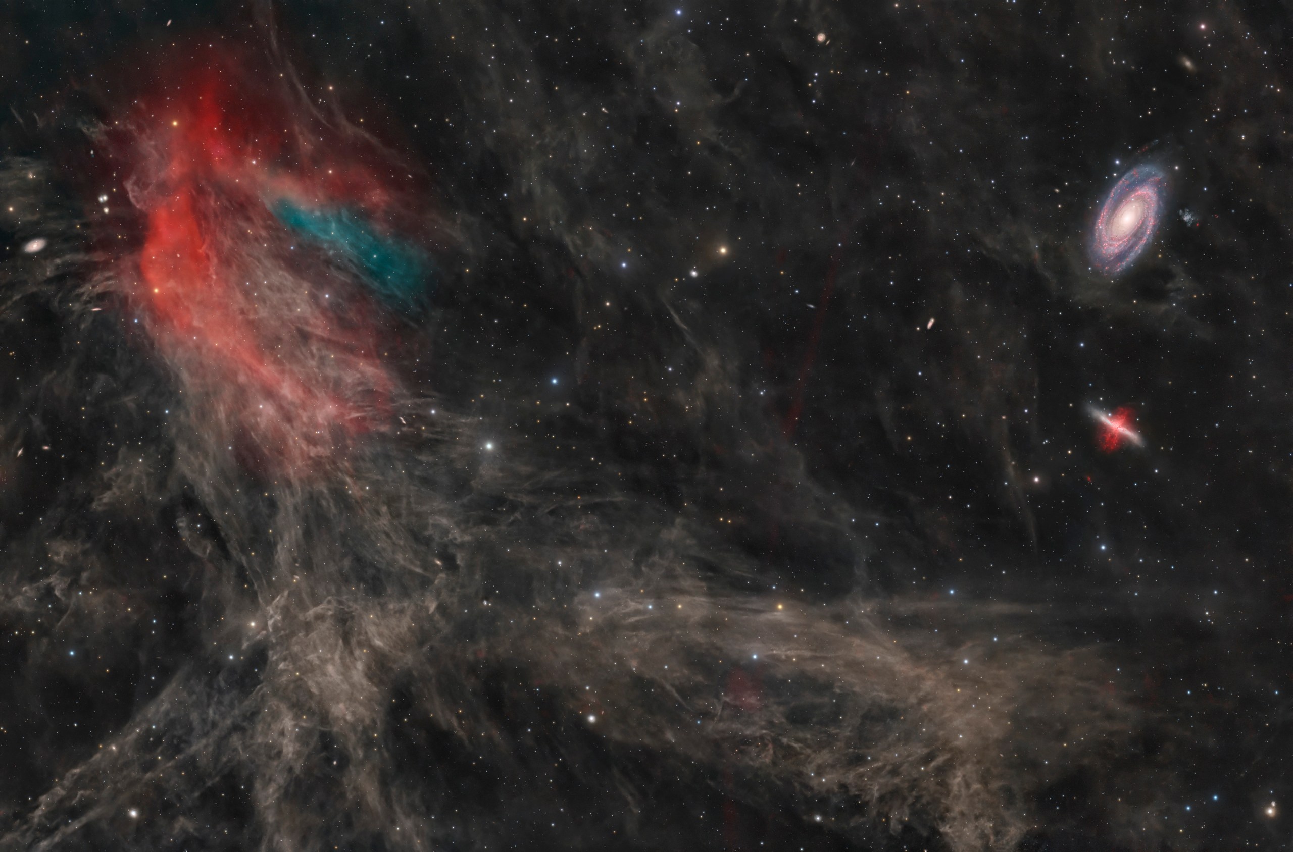 A dark starfield is veined with faint, wispy brown clouds. At left, a bright patch glows red and teal; at upper right sit a bright face-on spiral galaxy and a smaller, cigar-shaped reddish galaxy.