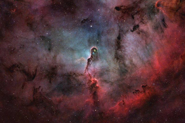 A dark, twisting column of dust with glowing pink edges curls up from the lower part of the frame toward a small, bright knot near the center. It sits amid vast clouds of deep red and dusky blue-gray gas, sprinkled with hundreds of stars across the field.