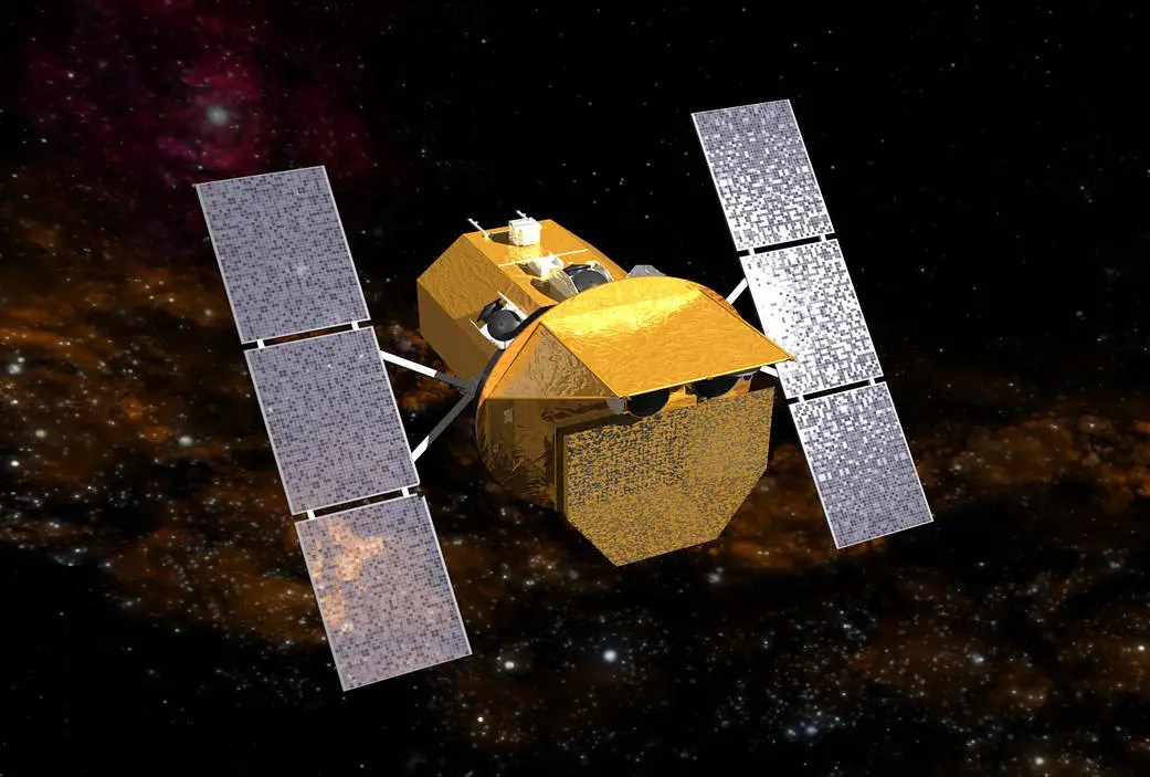 A gold-foil-wrapped satellite with two long rectangular solar panels extending from either side sits at the center of the frame, angled slightly toward the viewer. Small dark instruments and antennas cluster on its upper surface, and the spacecraft is set against a dense, glowing orange-brown starfield with a patch of pink and red nebulosity in the upper left.