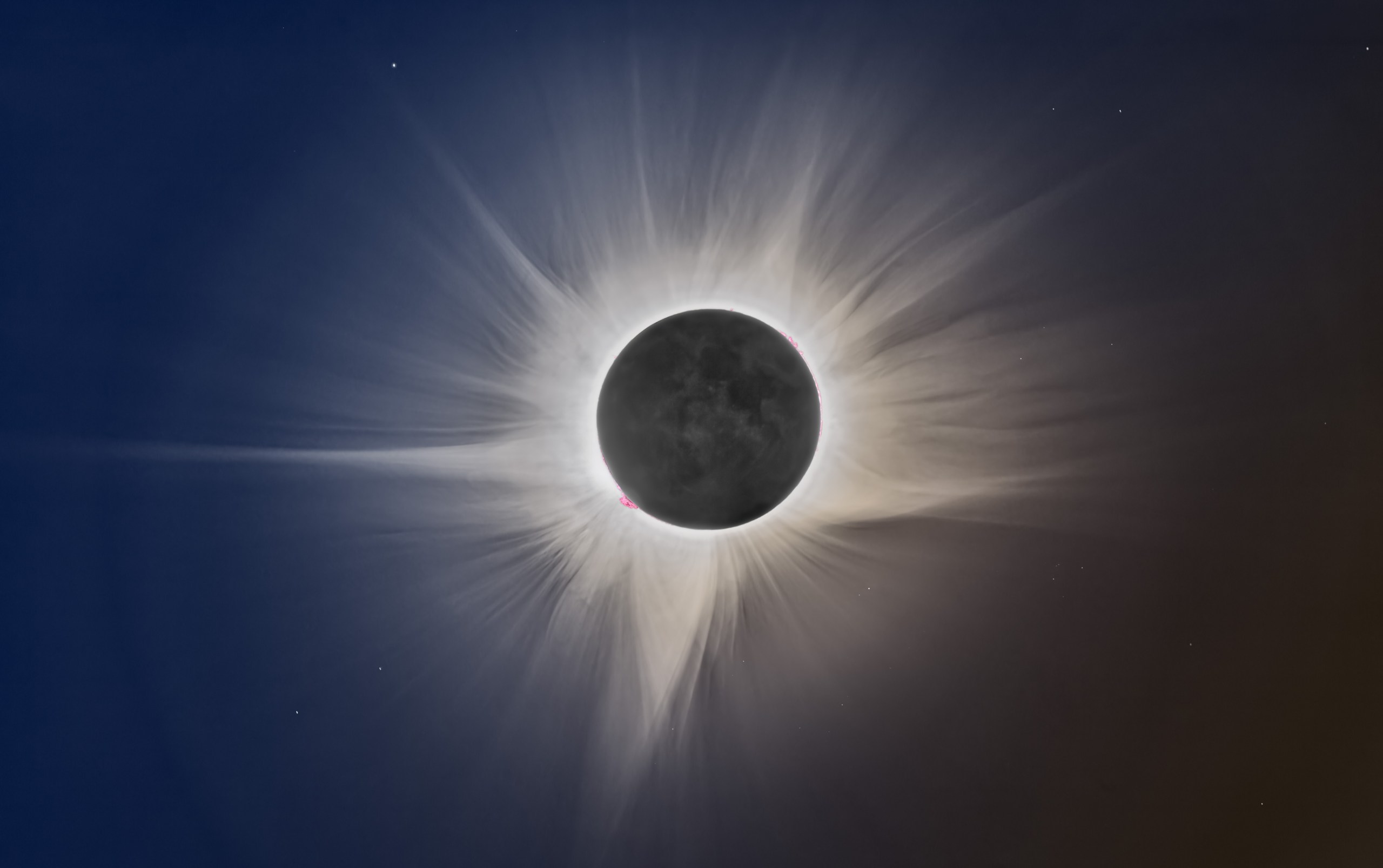 A black circle sits at the center of the frame, ringed by a bright white glow with wispy, feathery rays streaming outward in every direction like a spiky halo. Tiny specks of pink peek out along the edge of the dark circle. The background sky shifts from deep blue on the left to a warm brownish-orange on the right, with a few faint stars scattered here and there.