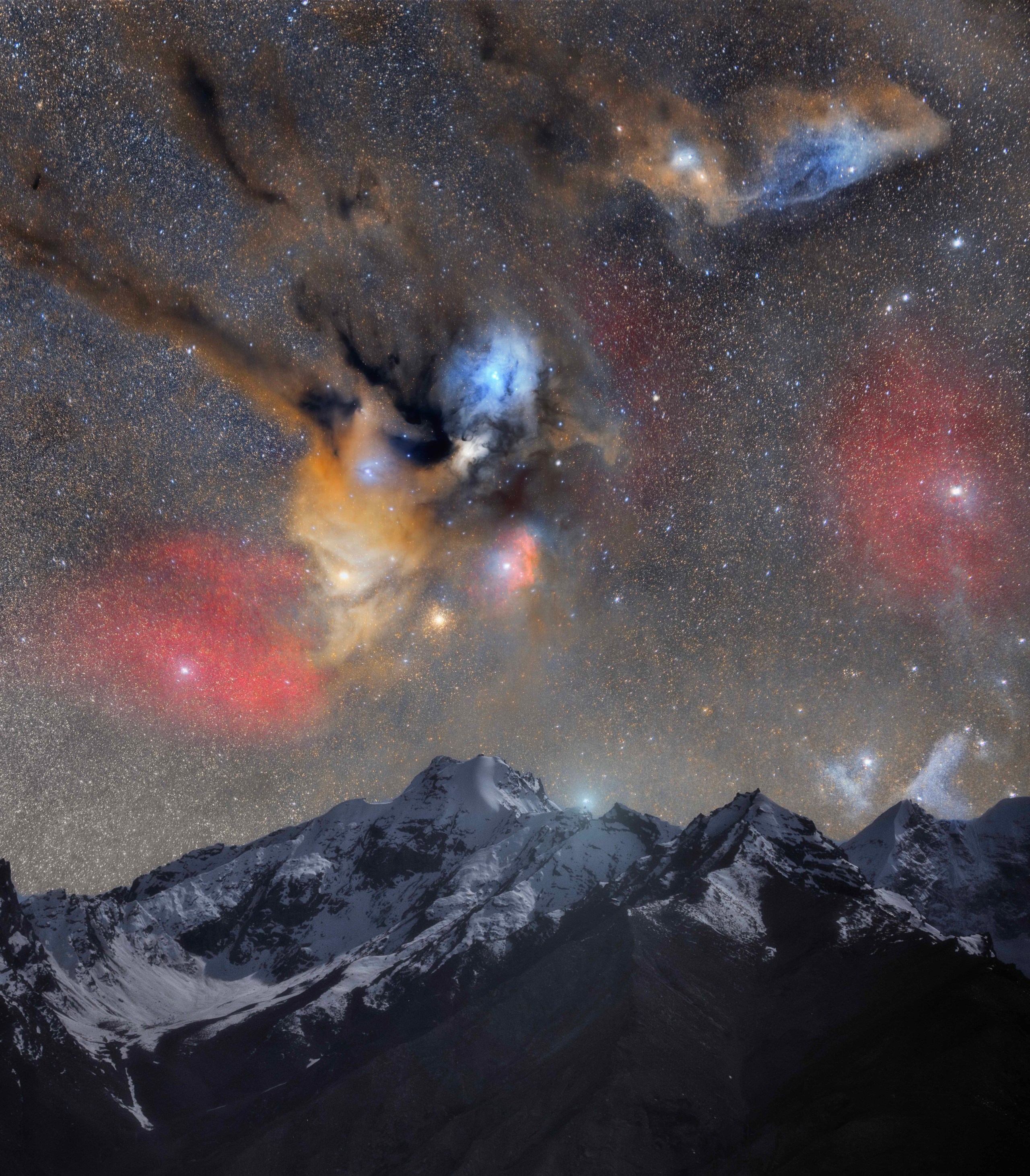 A jagged, snow-covered mountain range sits beneath a dense, star-filled sky. Above the peaks, patches of orange, red, and blue glow softly amid dark, wispy clouds of dust, with a dense cluster of yellow stars and a bright orange-white star shining just above the highest summit.