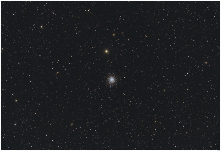 A telescopic photograph of M30, a globular cluster appearing as a compact, dense ball of white and blue-white stars near the center of the image, with a bright yellow-orange foreground star visible just above it. The cluster is set against a black sky scattered with numerous orange, yellow, and white foreground stars of varying brightness.