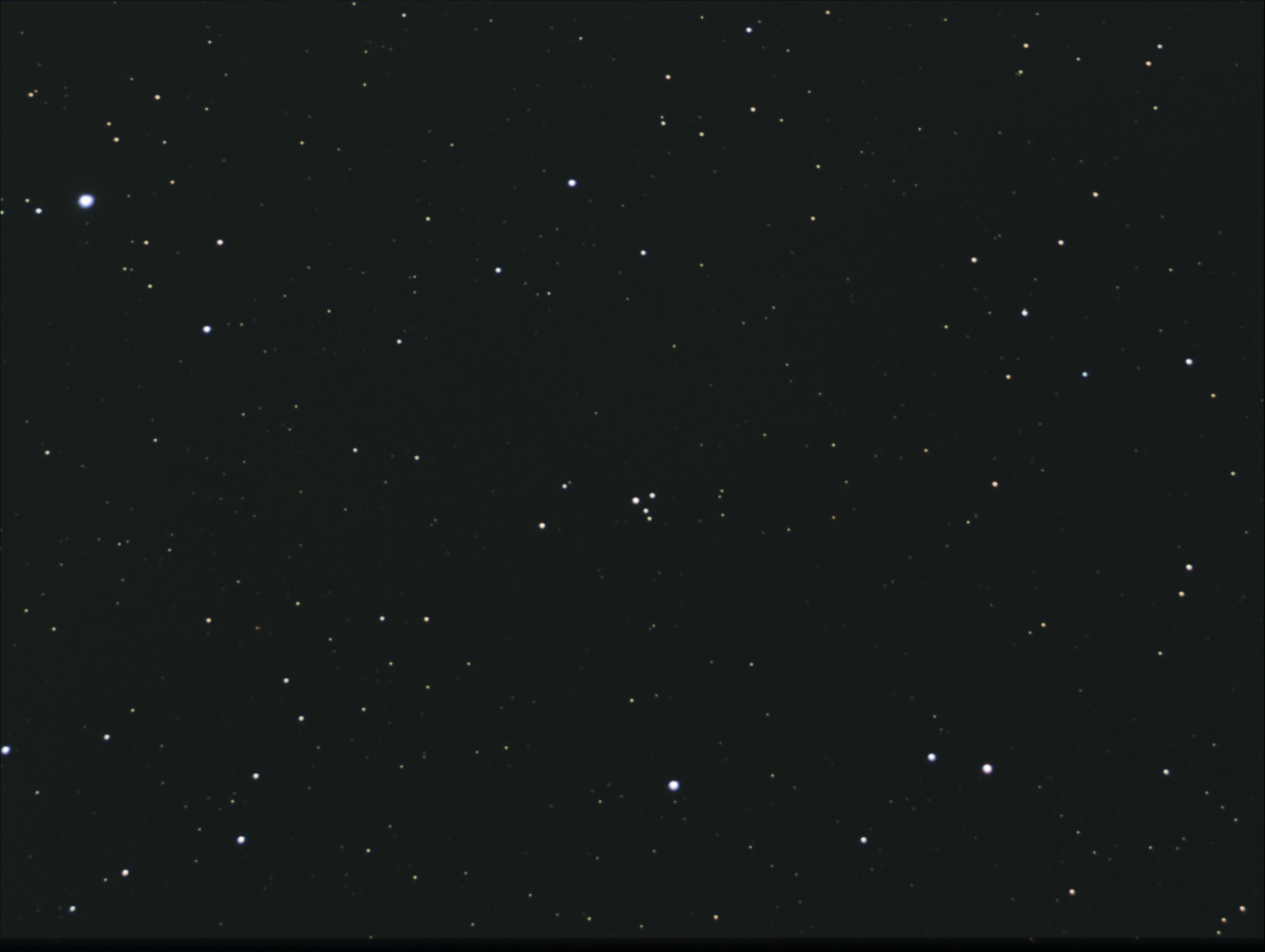 A telescopic photograph showing M73, a small asterism of four stars arranged in a tight Y-shaped grouping near the center of the image, set against a sparse star field of faint orange and white points on a black background.