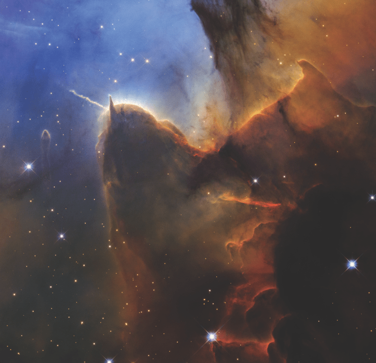 A detailed telescope image of a star-forming region, showing dramatic pillars and billowing clouds of gas and dust in vivid shades of orange, red, and brown, contrasting with cooler blue nebulosity in the upper left. A tall, dark pillar dominates the center with a bright jet of material streaming from its tip, illuminated by nearby stars. Smaller pillars and sculpted gas structures are visible throughout, and several bright foreground stars with diffraction spikes are scattered across the scene.