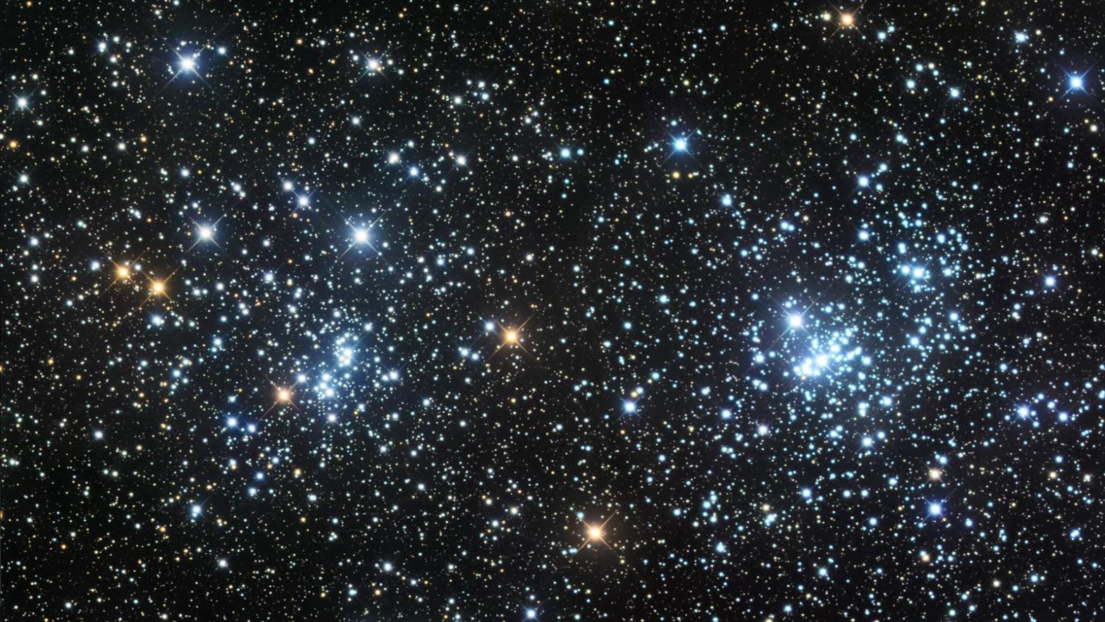 Photograph of the Double Cluster, showing two dense groupings of blue-white and orange stars side by side against a black sky thickly populated with fainter background stars, with the brightest stars in each cluster showing prominent diffraction spikes.