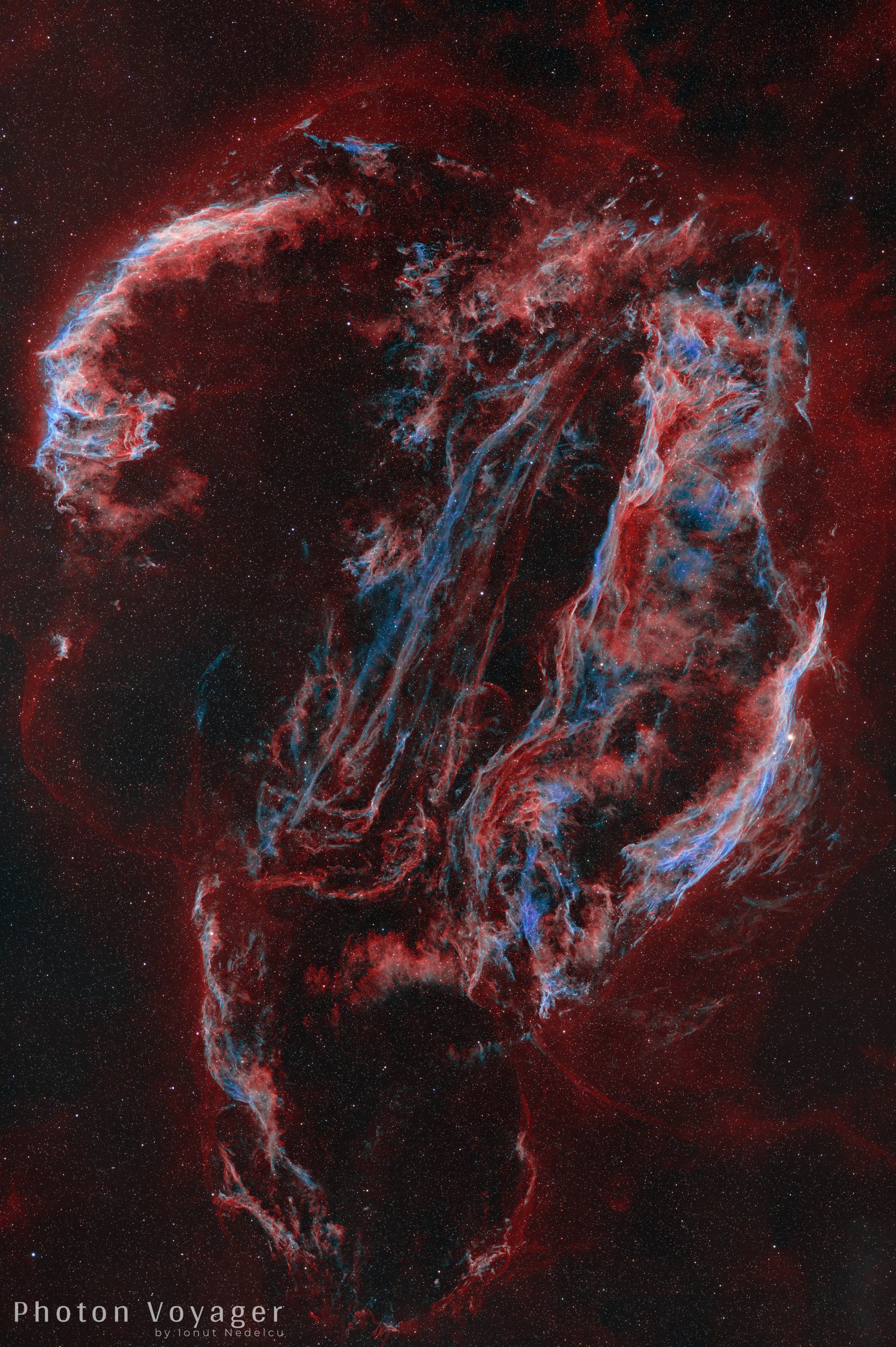 A tall, roughly oval ring of tangled, thread-like clouds fills the frame against a dark red haze sprinkled with tiny stars. The strands glow red with streaks of pale blue and white, brightest along a curved arc at upper left, a long sweeping arc at right, and a pair of thin, nearly straight streaks running diagonally through the middle, while a fainter, looser loop trails off toward the bottom.