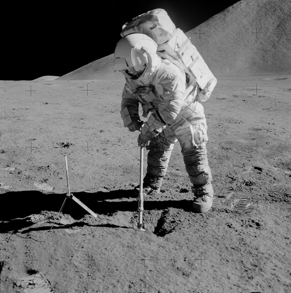 Apollo 15 astronaut James Irwin prepares to drill 2.4-meter deep into the surface to collect a rock sample.