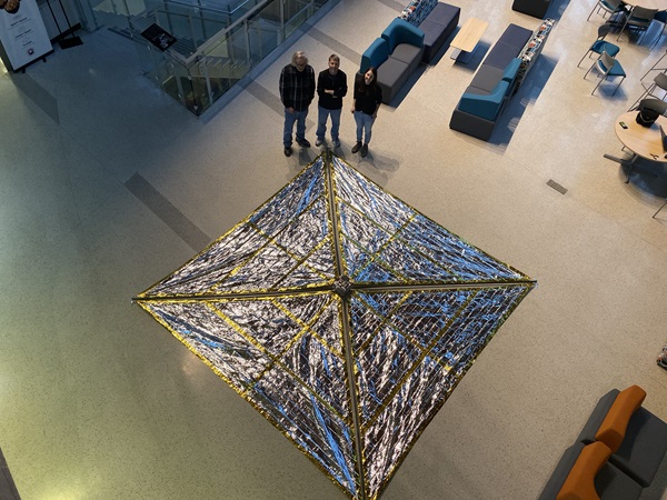 Three people with a fully-deployed drag sail in a building atrium, as seen from a drone