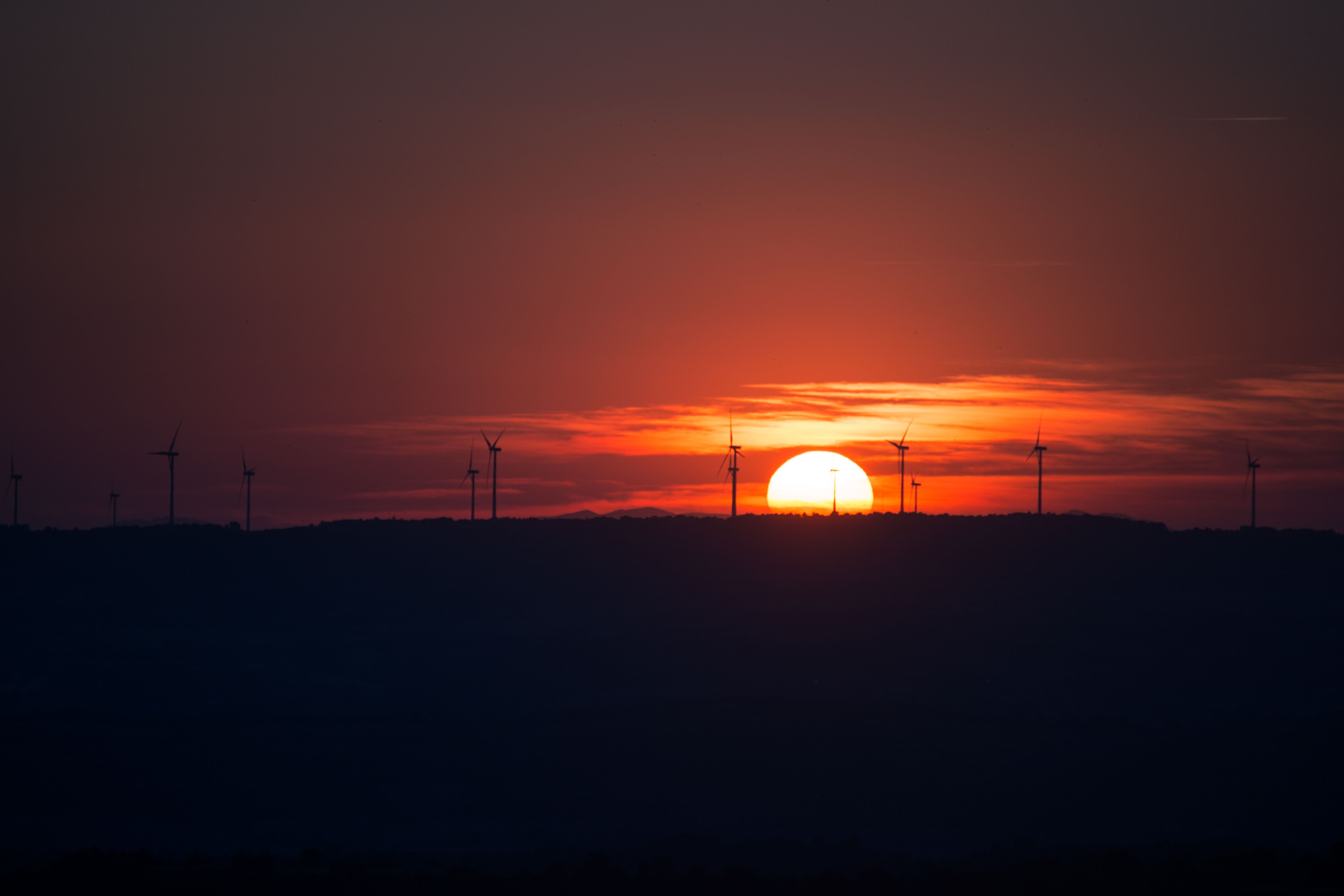 Słońce zachodzi za farmą wiatrową, rzucając pomarańczową poświatę na horyzont i kształtując turbiny wiatrowe