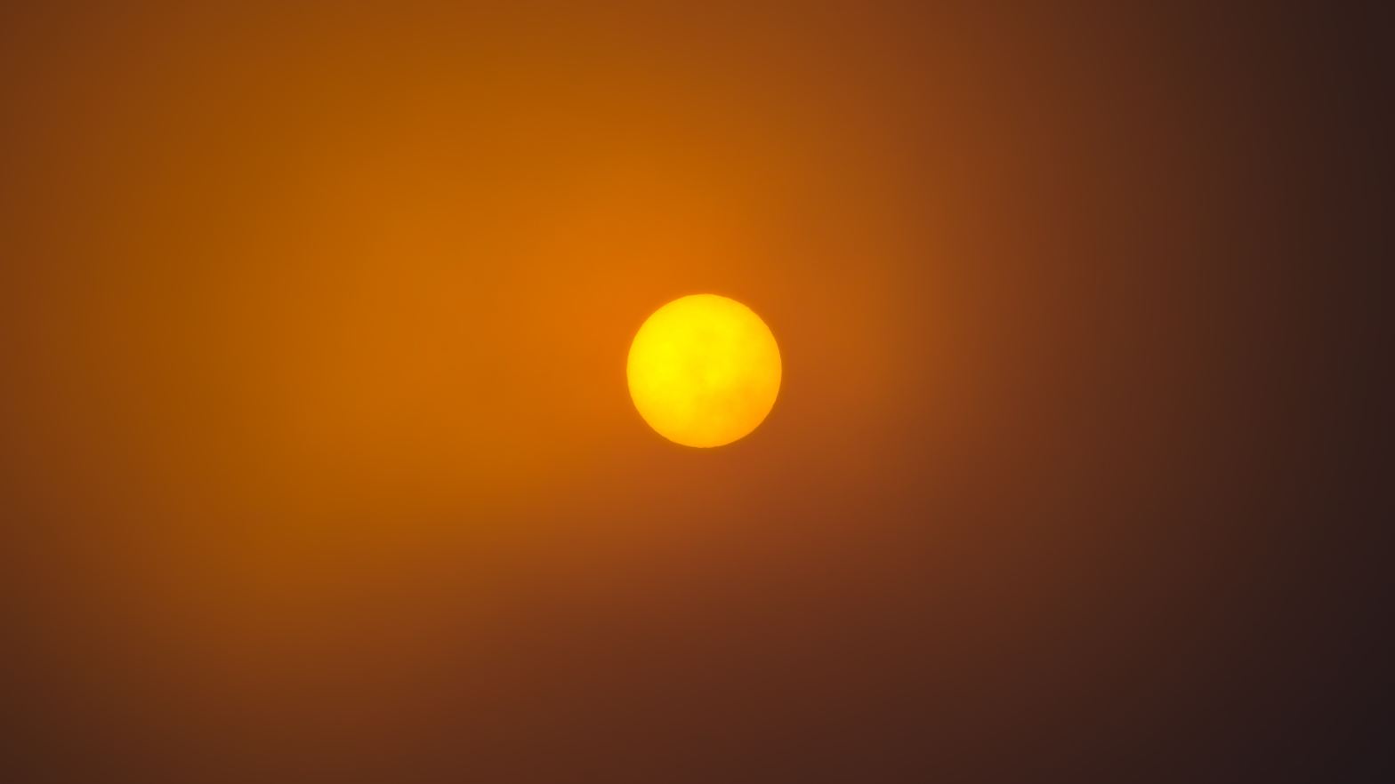 The orange disk of the sun, darkened by smoke or clouds