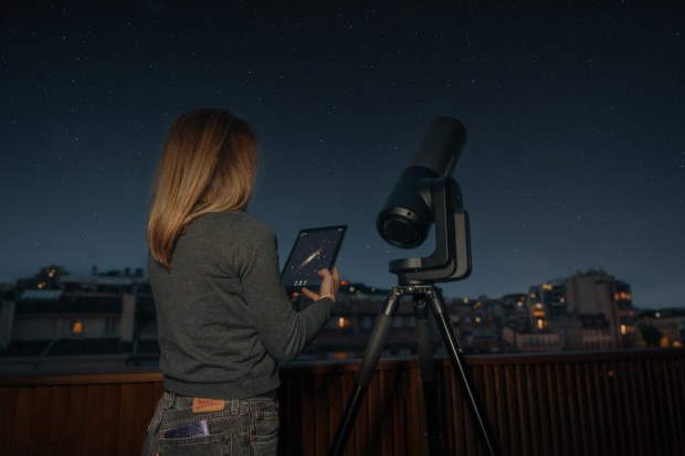 A woman using the Unistellar app on a device to operate the Unistellar eQuinox 2 telescope.