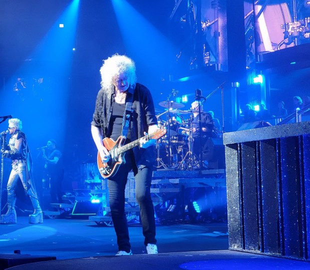 Brian May solos during Queen's 2023 Rhapsody Tour in Chicago, with Adam Lambert and Roger Taylor in the background.