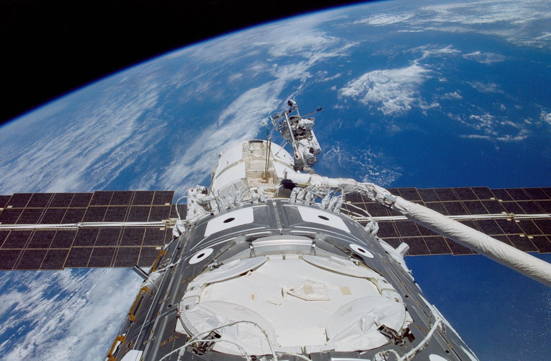 James H. Newman (right) and Jerry L. Ross (lower left) work on the recently-connected Russian-built FGB Module (Zarya) and the United States-built Unity Module in 1998. The photograph was taken out the window of the Earth-orbiting Space Shuttle Endeavour. Credit: NASA.