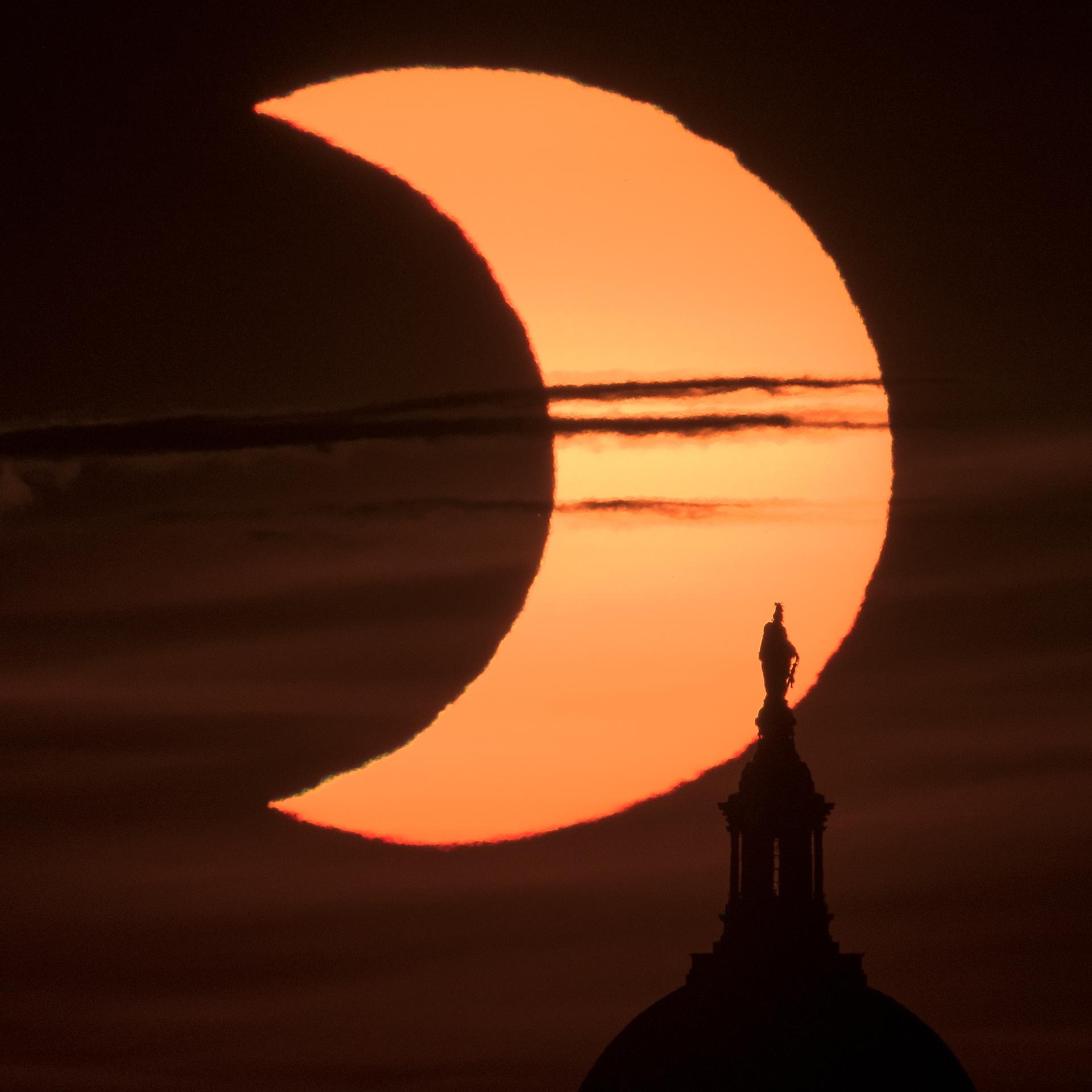 A partial solar eclipse is seen as the sun rises behind the Statue of Freedom atop the United States Capitol Building, Thursday, June 10, 2021, as seen from Arlington, Virginia. Credit: NASA/Bill Ingalls