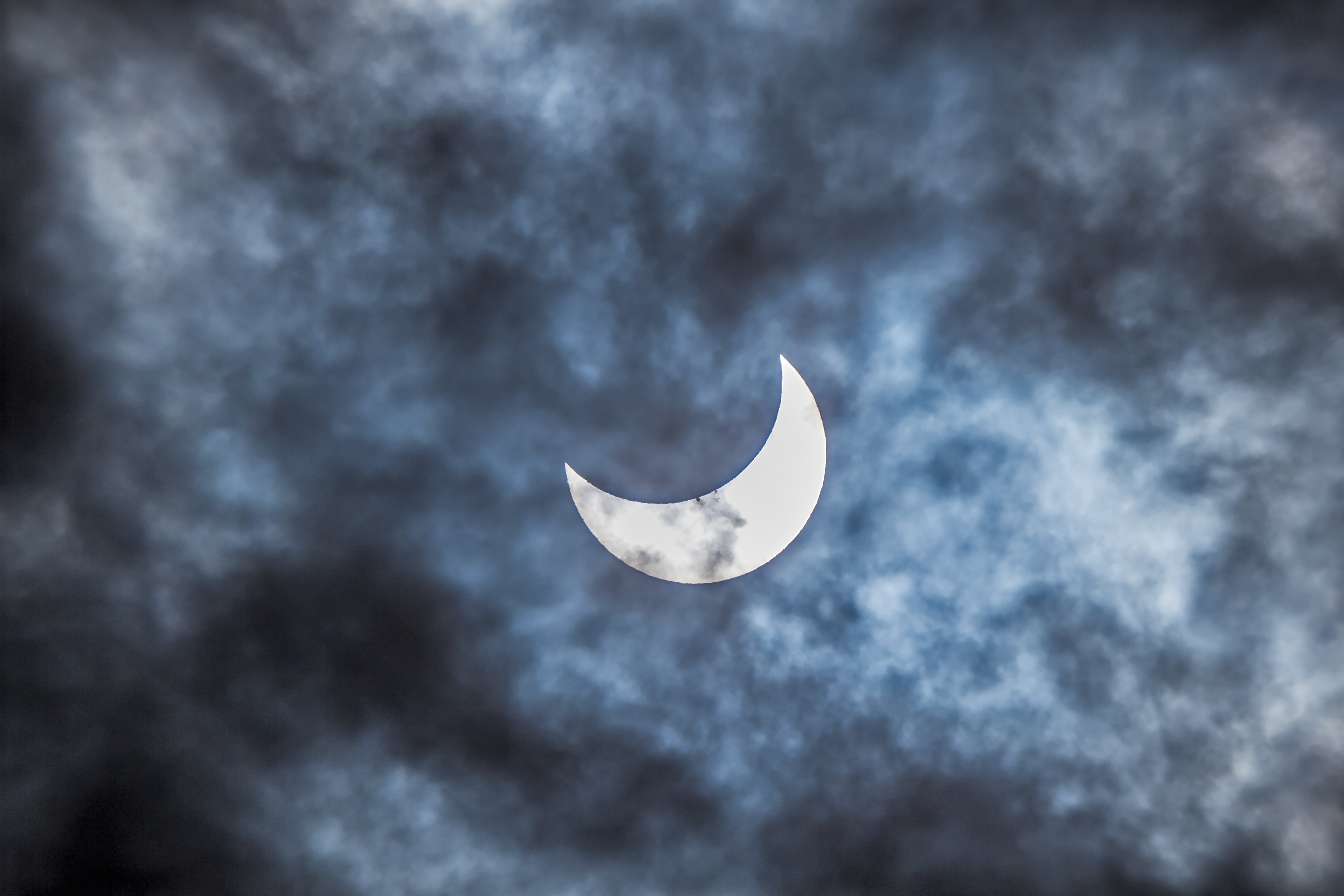 Not all clouds spell disaster for a total solar eclipse. This shot shows a partial eclipse underway behind cloud cover. A group of sunspots is visible near the edge of the lunar disk. 