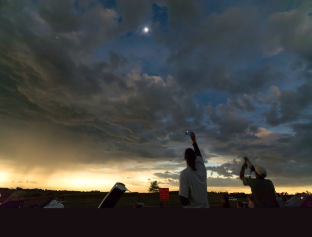 The glow of twilight — as well as rain showers — is visible on the horizon as this eclipse-viewing party spots their target in a break in the clouds on Aug. 17, 2021. 